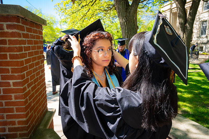 A girl helping another girl with her graduation cap. Links to Gifts of Life Insurance