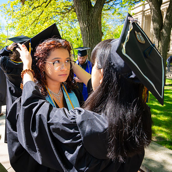 A graduating student helping her classmate straighten her graduation cap